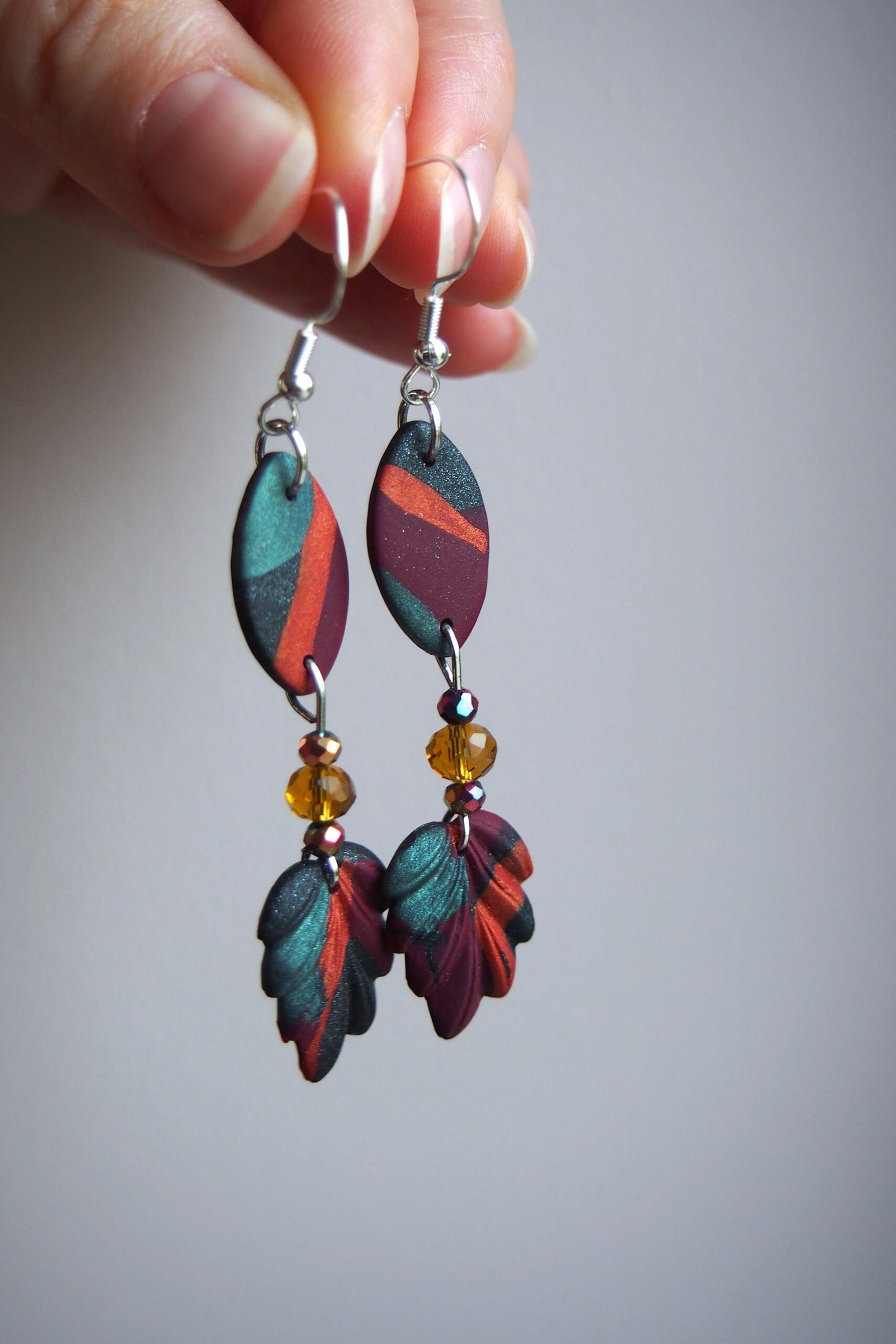 Handmade nature-inspired mismatch polymer clay dangle earrings featuring unique multicolored abstract designs. Accented with small amber beads and leaf shapes, these colorful, artsy statement earrings offer a whimsical & unique touch to any outfit.